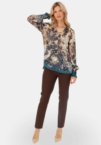 Kwiatowa bluzka w stonowanych, ziemistych odcieniach, z długimi rękawami i falbankami przy mankietach oraz dekoltem w kształcie litery V. Zestawiona z brązowymi dopasowanymi spodniami i cielistymi szpilkami.