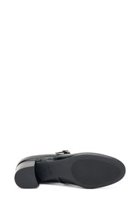 Zapato de cuero negro con una textura suave, tacón de bloque de altura media y un sutil detalle de correa. La suela presenta un patrón de tracción para un mejor agarre.