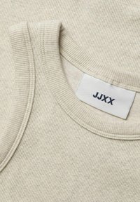 Beige ribbestrikket tanktopp med rund hals, som viser et teksturert stoff. Et merke med "JJXX" er synlig nær halslinjen.