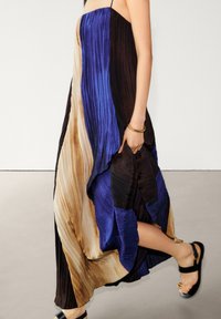 Maxikleid mit plissiertem Stoff in Blau-, Braun- und Beigetönen sowie Spaghettiträgern. Der Stoff hat eine glatte Textur und ein fließendes Design.