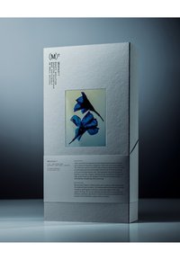 Boîte beauté édition limitée avec une finition en papier blanc texturé, présentant un motif floral bleu encadré et une typographie noire élégante sur le côté.