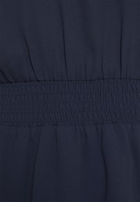 Mörkblått tyg med en slät struktur, som har dragband i midjan. Materialet flödar mjukt med en ljus glans.