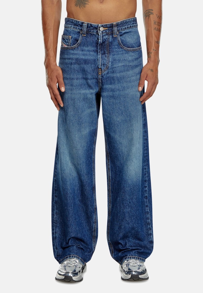 Jean en denim bleu ample avec un effet de lavage plus clair, poches avant, coutures surélevées et fermeture à bouton à la taille.