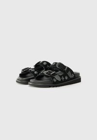 Black sandals featuring double straps, buckles, and embossed patterns with a textured rubber sole and treaded outsole.