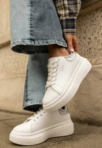 Białe skórzane sneakersy z grubą, białą podeszwą, z okrąłym noskiem, sznurowanym zapięciem i minimalistycznym logo z boku.
