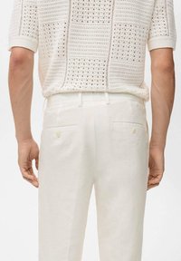 White linen pants with two back pockets and button accents, paired with a textured, short-sleeve knitted shirt in a light shade.