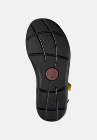 Black rubber shoe sole with textured grip pattern and molded details. Features a round red tag marked '38.' Designed for stability and traction.