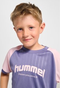 Lila och rosa tränings-T-shirt med rund halsringning, korta ärmar och vertikala ränder; har "hummel"-logotyp i vitt.