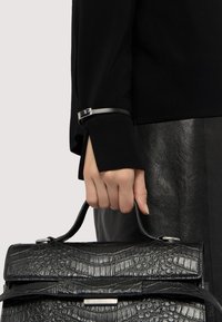 Borsa in pelle nera con stampa a coccodrillo tenuta in mano, dotata di una chiusura in metallo silver e una finitura texturizzata. Visibile una parte superiore scura e una gonna in pelle.