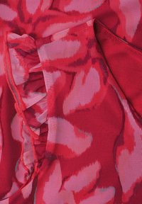 Gros plan d’un tissu floral rouge et rose avec un détail de couture froncée sur un matériau léger texturé.