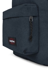 Mörkblå tygryggsäck med en ficka fram med dragkedja, texturerad yta och en svart logolapp med röda accenter.