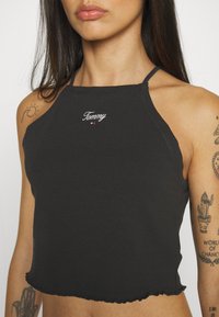 Black cotton halter top with frayed hem, featuring white "Tommy" embroidery at the neckline and adjustable straps.
