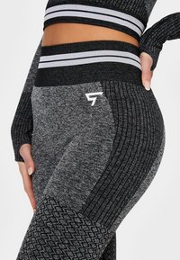 Vysoké černé a šedé legíny s ribbed texturou, zdobné akcenty a logem na straně. Design z pružného materiálu.