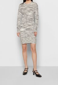 Långärmad klänning i ljusgrått med mörka horisontella ränder, figursydd, med ribbade krage, bärs med svarta slingback-klackar.