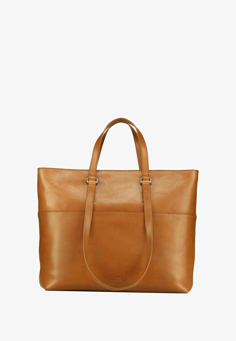 Sac fourre-tout en cuir tan avec deux poignées, une texture lisse, une poche frontale et un branding discret près de la base. Forme rectangulaire.