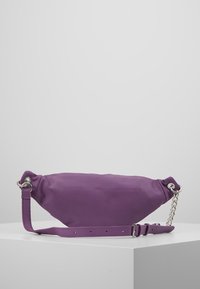 Fioletowa skórzana torebka o zaokrąglonym kształcie, z regulowanym paskiem i srebrnym akcentem w postaci łańcuszka. Gładka tekstura i minimalistyczny design.