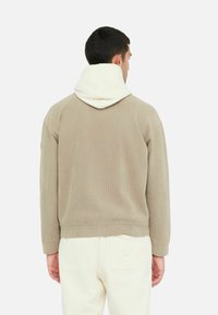 Brun fløjlshoodie med hætte i cremefarvet bomuldsfor. Har en afslappet pasform, ribbede manchetter og en cropped kant. Rent design uden synlige logoer.