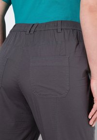 Šedé kalhoty s elastickým pasem mají velkou zadní kapsu v obdélníkovém tvaru, tónové švy a hladkou texturu látky. Neformální design.