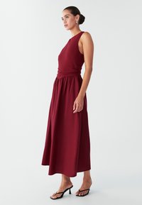 Burgundiipunane varrukateta kleit, millel on vormitud ülakeha ja kogutud vöökoht. Voogav, pahkluud kattev seelik. Kandmisega mustad kontsakingad.