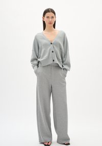 Gray knitted cardigan with a V-neck and five black buttons, paired with wide-leg gray pants, both made of soft, textured fabric.