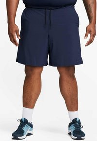 Navy athletic shorts with an elastic waistband and drawstring, featuring side pockets. Paired with navy and light blue sneakers and white socks.