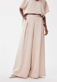 Pantalons beige à jambes larges avec plis et taille élastique, associés à un haut ample assorti. Tissu lisse et léger.