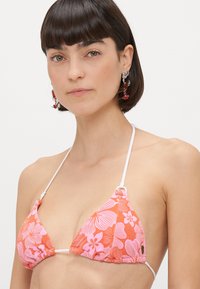 Top de bikini triangular din țesătură portocalie, cu modele florale roz, bretele albe ajustabile și suprafață texturată.
