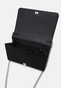 Svart faux läderväska med en slät yta, kedjesnurra och magnetisk stängning. Insidan har ett zipfack och kortfack.