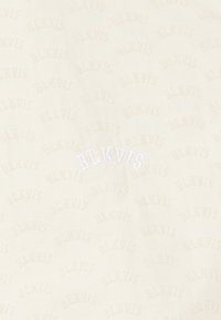 Tissu couleur crème avec un motif en relief répétitif portant "BLKVIS." Présente un logo brodé blanc légèrement décentré. Texture douce.