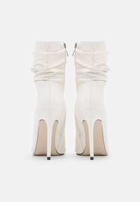 Bottes blanches à talons hauts avec tissu froncé, texture lisse, et fermetures éclair à l'arrière ; dotées d'un bout pointu élégant et d'un talon stilettos fin.