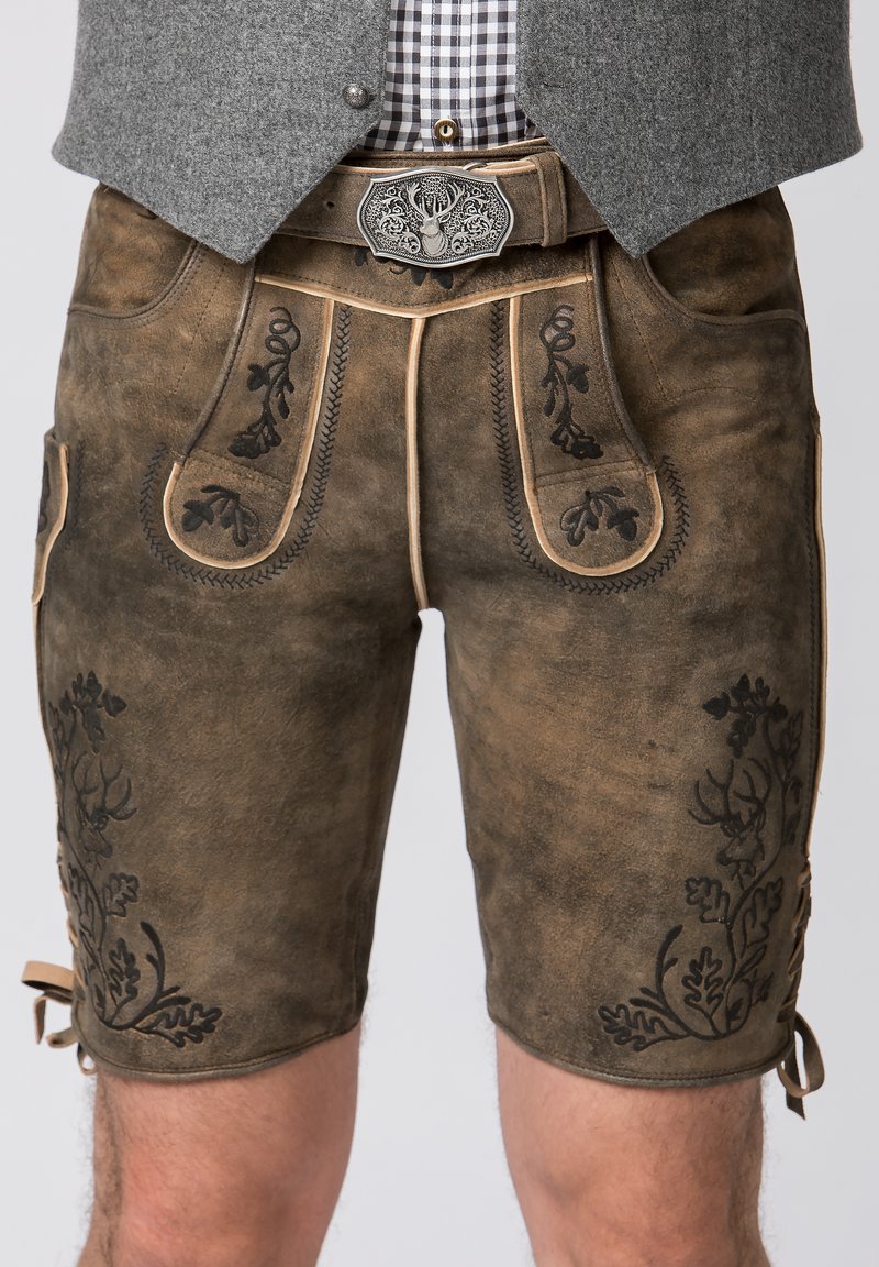 Skórzane lederhosen w kolorze brązowym z czarnym haftem kwiatowym i kontrastującymi szwami. Posiada boczne kieszenie oraz wiązania na dole do regulacji.