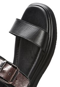 Sandalo in pelle nera con una larga fascia e fibbia metallica lucida. Suola spessa con una finitura testurizzata. Design confortevole e contemporaneo.