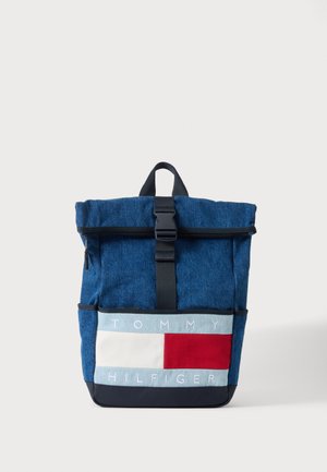 Blauwe stoffen rugzak met zwarte gespsluiting, grote voorvak en Tommy Hilfiger-logo in wit, rood en blauw paneel aan de voorkant.
