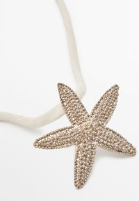 Søstarsformet vedhæng i sølvtoner, struktureret med små perler, fastgjort til et lys beige stofsnor.