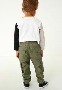 Camicia di cotone a maniche lunghe con accenti grigi, neri e gialli, abbinata a pantaloni cargo verdi con tasche laterali e polsini elasticizzati.