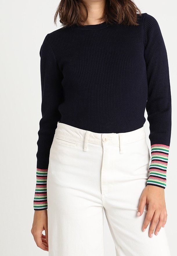 Mörkblå randig tröja med lång ärm och flerfärgade randiga muddar, kombinerad med högmidjade vita byxor. Strukturerad tyg.