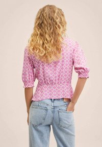 Blouse rose à motifs avec manches bouffantes, présentant un design géométrique et une taille froncée. Associée à un jean taille haute bleu clair.