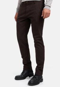 Pantalones slim-fit de color marrón oscuro, fabricados con un tejido resistente, que presentan un clásico diseño de cinco bolsillos y un cierre de cremallera con botón.