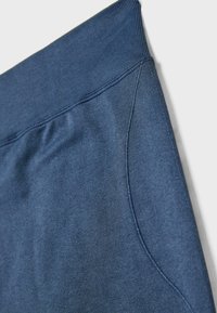 Tamne plave trenirke s rebrastim pojasom, glatkom teksturom i bočnom džepom s kontrastnim šavovima. Meki, rastezljivi materijal.