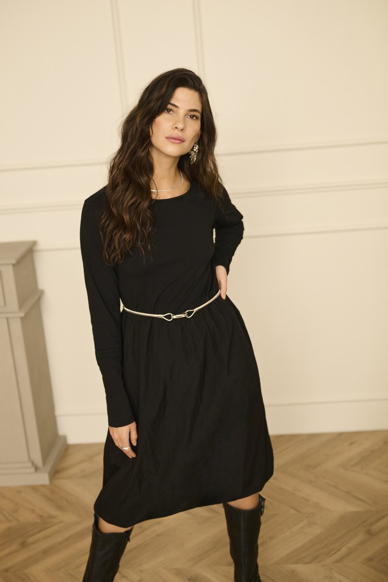 Crna haljina dugih rukava s strukiranim pojasom, teksturirana tkanina i srebrni remen, uparena s crnim čizmama do koljena na drvenom podu.