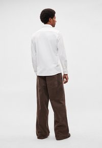 Valge pikkade varrukatega triiksärk kraega, kombineeritud lahtiste pruunide nandipükstega, millel on tagataskud. Sile tekstuur ja lõdvestunud istuvus.