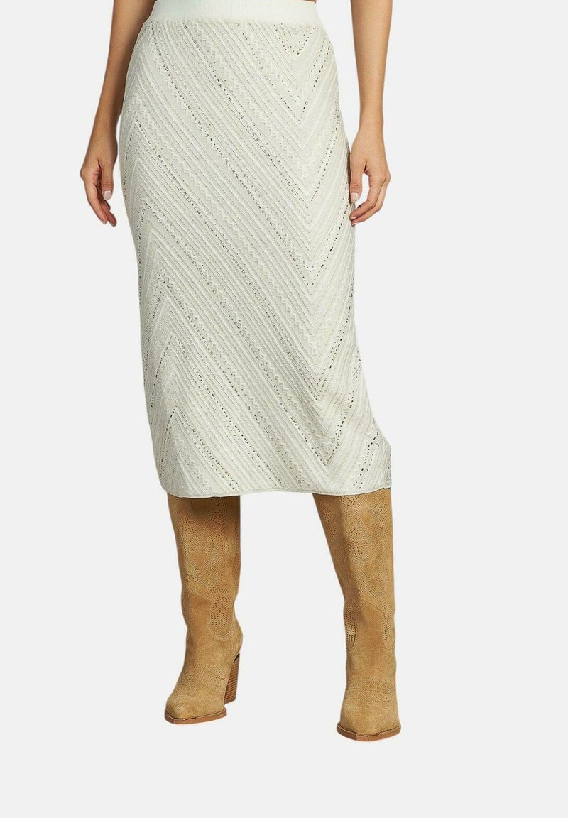 Jupe midi en tricot de couleur beige clair avec un motif en chevron, dotée d'une taille ajustée et d'une surface texturée, associée à des bottes marron clair jusqu'aux genoux.
