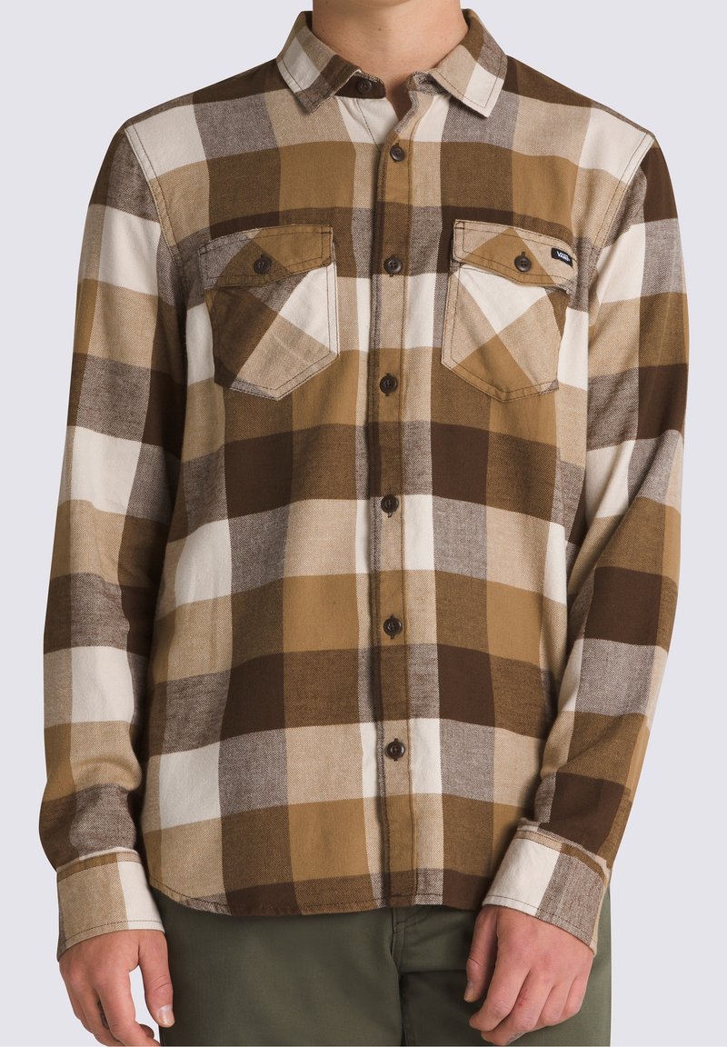 Homme portant une chemise à carreaux marron, beige et blanche à boutons, avec deux poches poitrine et des boutons foncés.