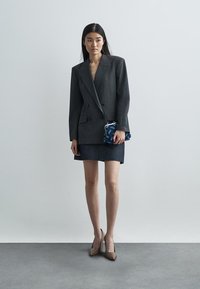 Grey pinstriped double-breasted blazer over a dark denim mini skirt, paired with beige heels and a patterned blue clutch.
