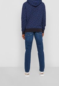 Felpa a mostre navy con cappuccio e polsini neri, abbinata a jeans blu e sneakers bianche con colori a contrasto. Outfit casual visto da dietro.