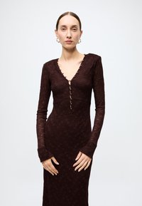 Burgundy lace dress with long sleeves, deep V-neck, and button accents down the front. Features a fitted silhouette and textured fabric.