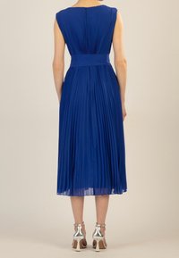 Pleated blue dress with a fitted waist and sleeveless design. Features a back zipper and falls to mid-calf. Worn with silver high-heeled shoes.