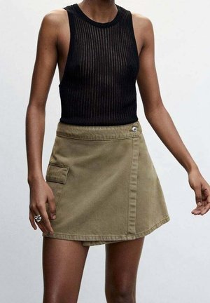 Débardeur noir côtelé associé à une jupe portefeuille kaki avec une poche avant et un détail de quincaillerie circulaire argentée.