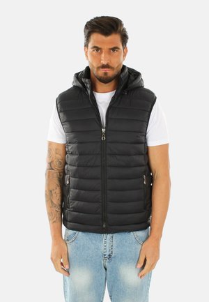 Gilet in piuma nero con cappuccio, chiusura con zip e tasche laterali. Fantasia trapuntata con una texture liscia, abbinato a una t-shirt bianca e jeans di denim.