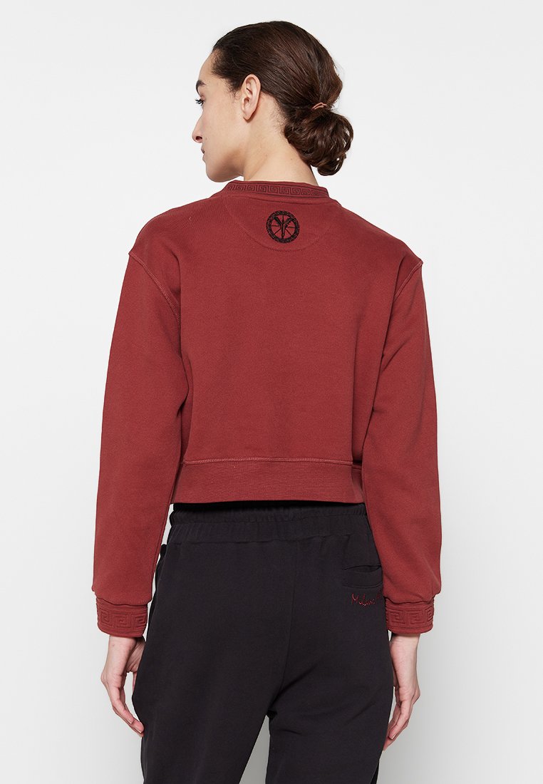Gekürzter, burgunderfarbener Sweatshirt mit langen Ärmeln. Besitzt eine strukturierte Naht am Hals und ein schwarzes Logo auf der Rückseite.